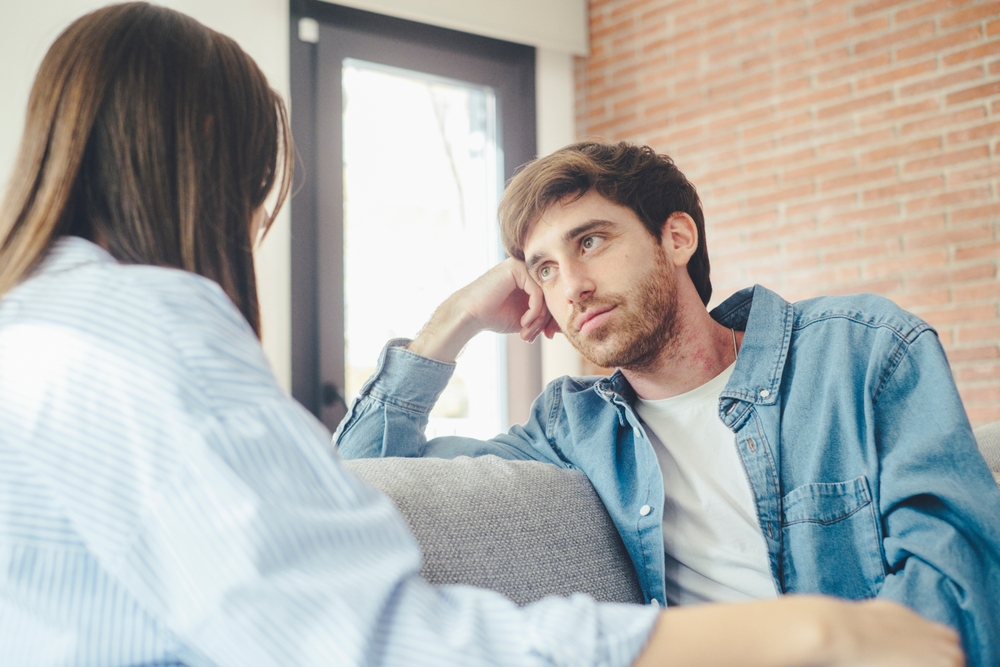 Serious young couple sitting together on sofa, talking about relationships