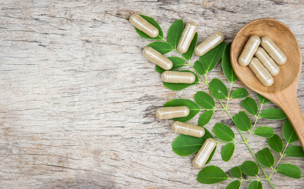 Herbal medicine in capsules from moringa leaf on rustic wooden table