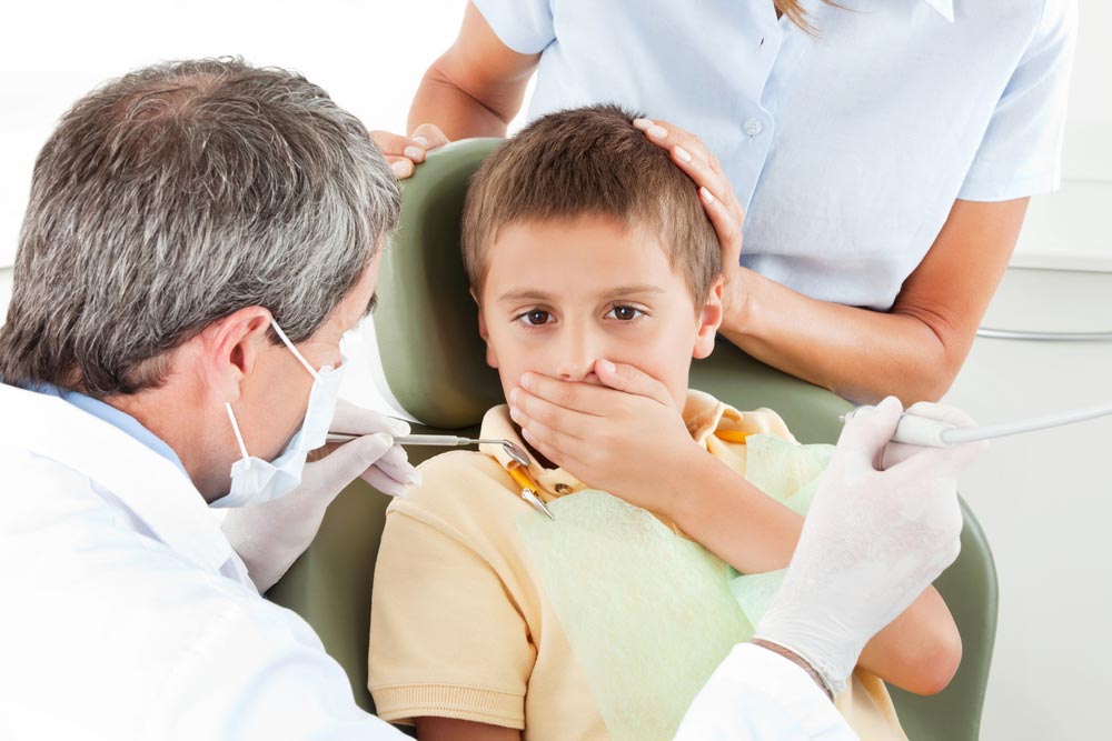 Boy at the dentist is scared and covers his mouth