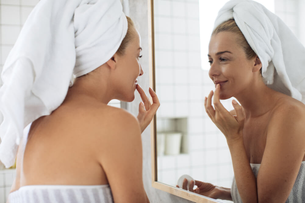 Pretty woman with towels putting balm on her lips after shower