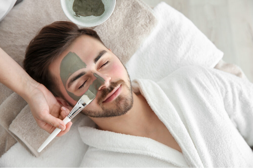 Cosmetologist applying mask on man face