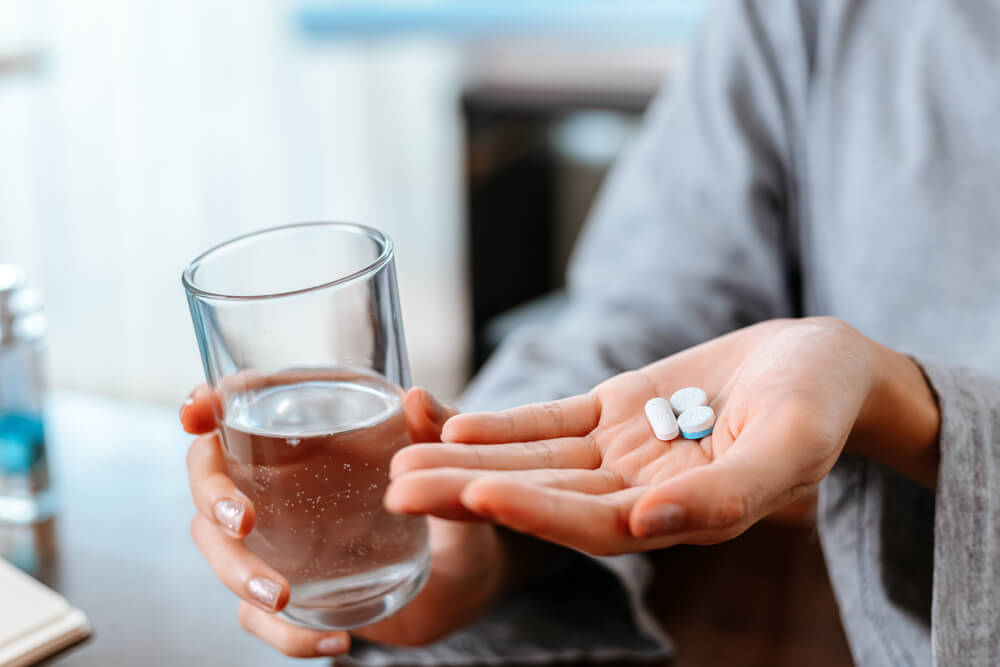 Woman with glass of water takes pill in hand