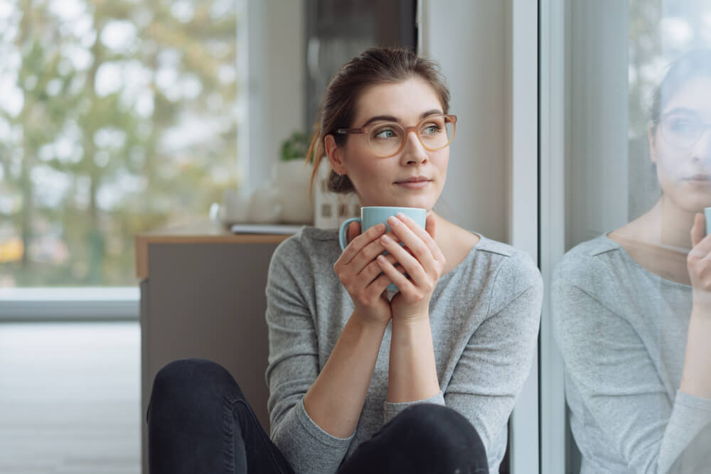 young woman sitting daydreaming with mug of coffee