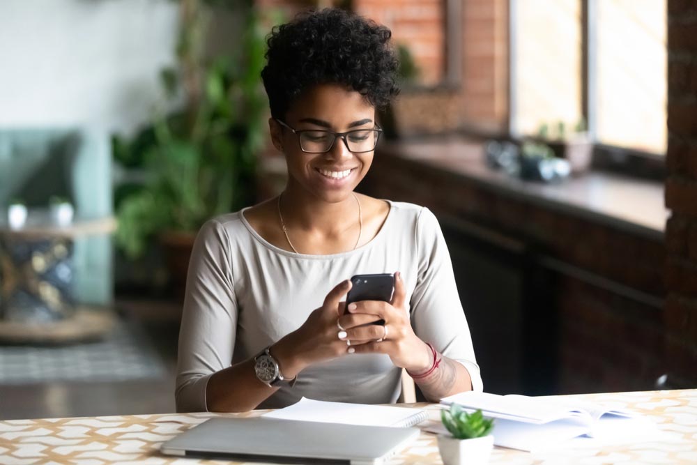 Cheerful woman sitting at table using cell phone