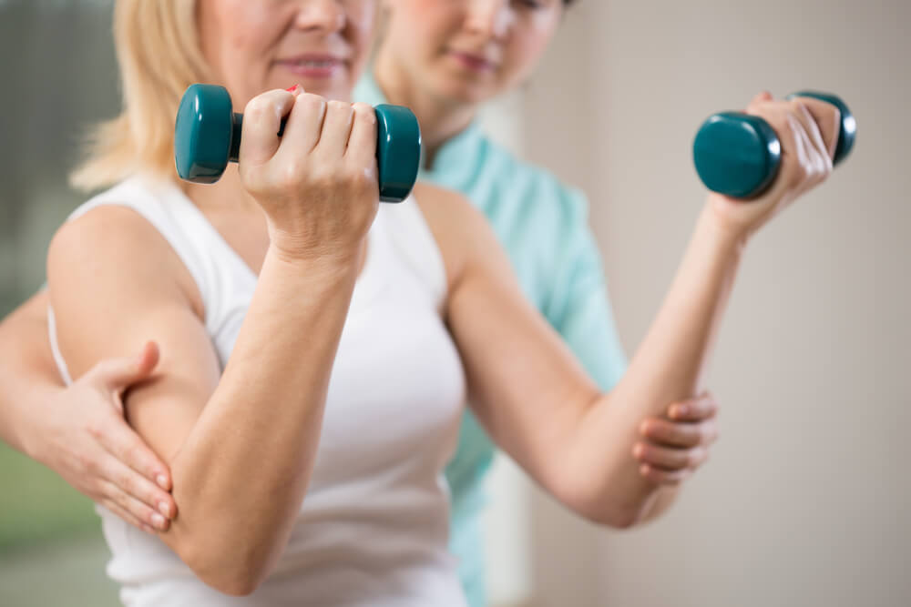 Woman exercising with dumbbells in rehabilitation clinic