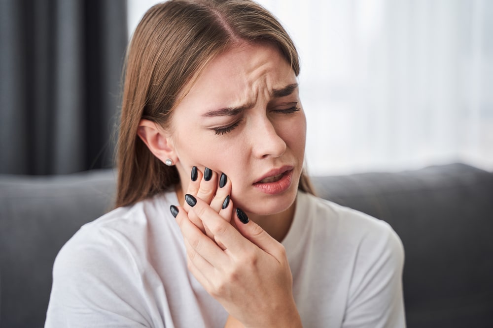Awful toothache. Frustrated young women suffering from toothache while sitting on the sofa at home. Stock photo