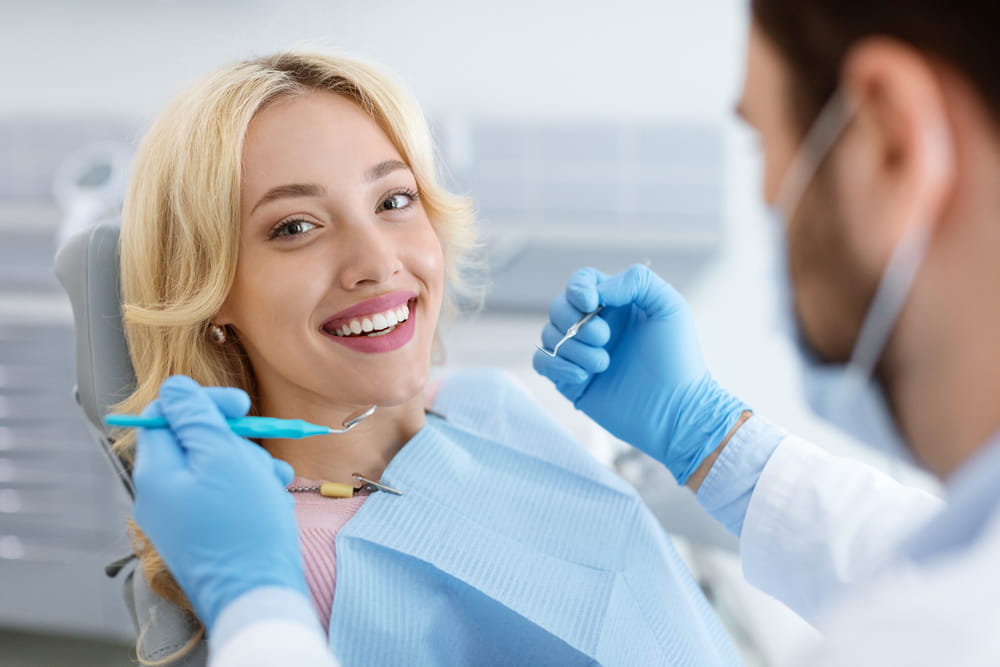 Closeup of man dentist in face mask doing treatment for patient cheerful young blonde lady