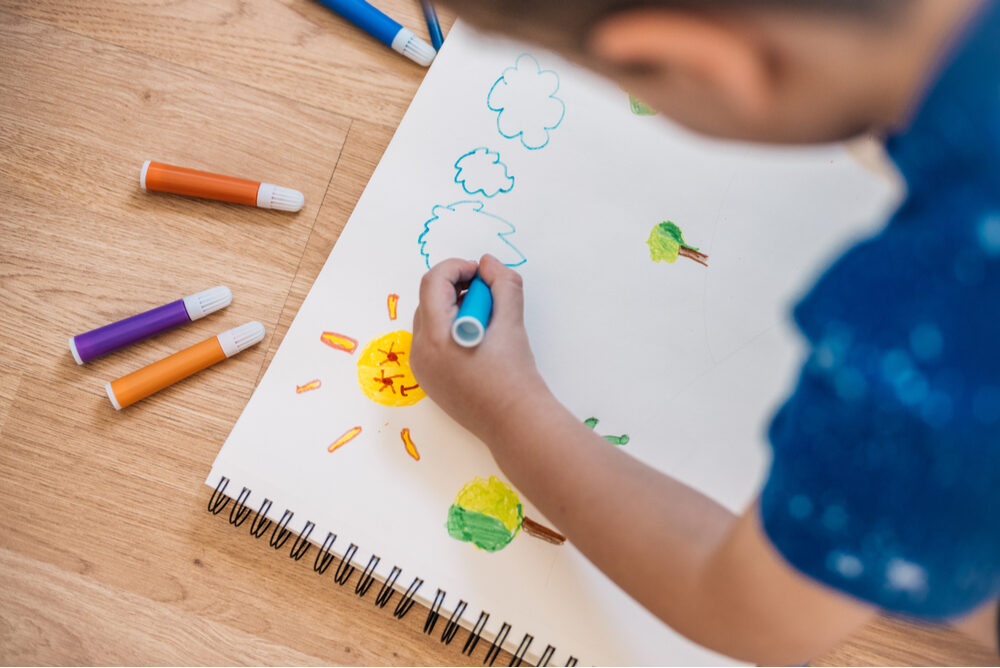 child drawing clouds with colored markers at home