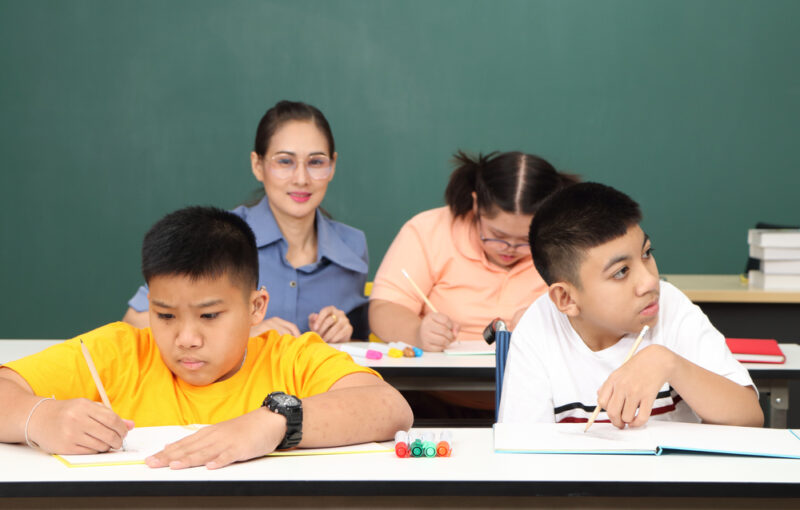 an autistic child learns to read, write, and train their hand and finger muscles with a teacher at their classroom desk