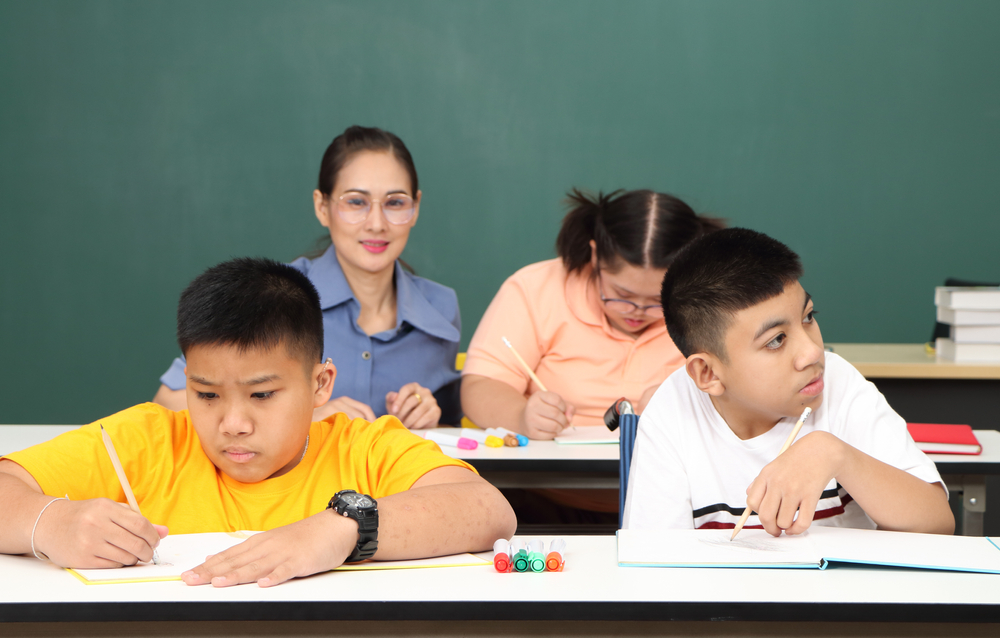 an autistic child learns to read, write, and train their hand and finger muscles with a teacher at their classroom desk