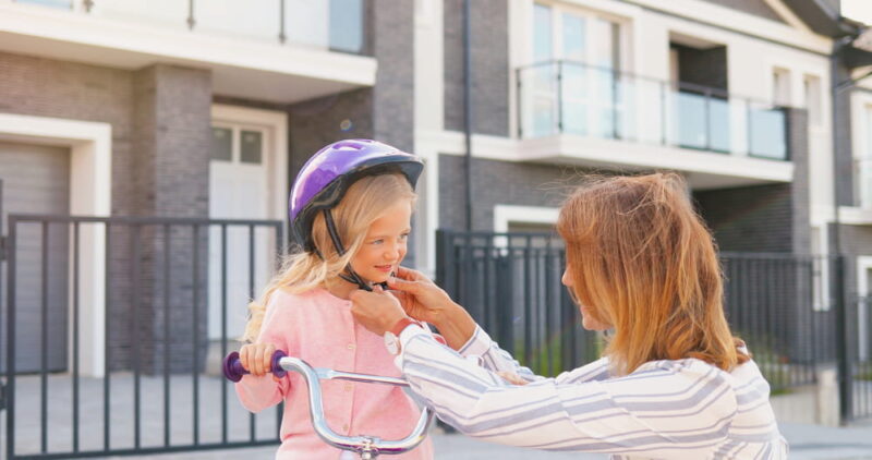 Close up of Caucasian mother wearing casque on small pretty girl and teaching ride on bike at street