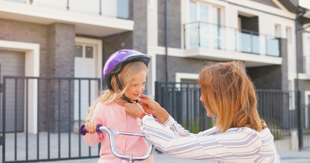 Close up of Caucasian mother wearing casque on small pretty girl and teaching ride on bike at street