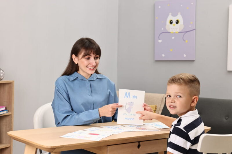 Smiling speech therapist working with little boy at table in autism treatment center