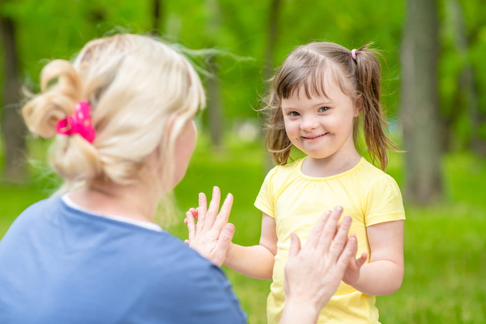 Little girl with syndrome down talks with her mother in a summer park