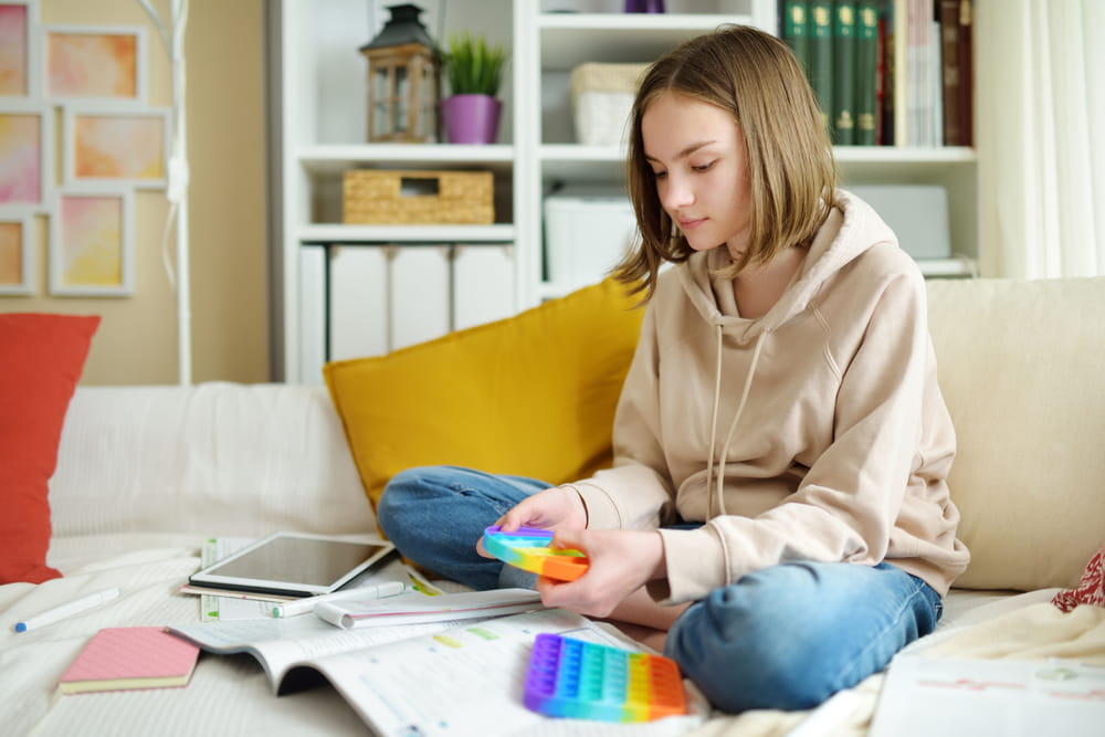 Teenage girl playing with rainbow pop-it fidget toy while studying at home
