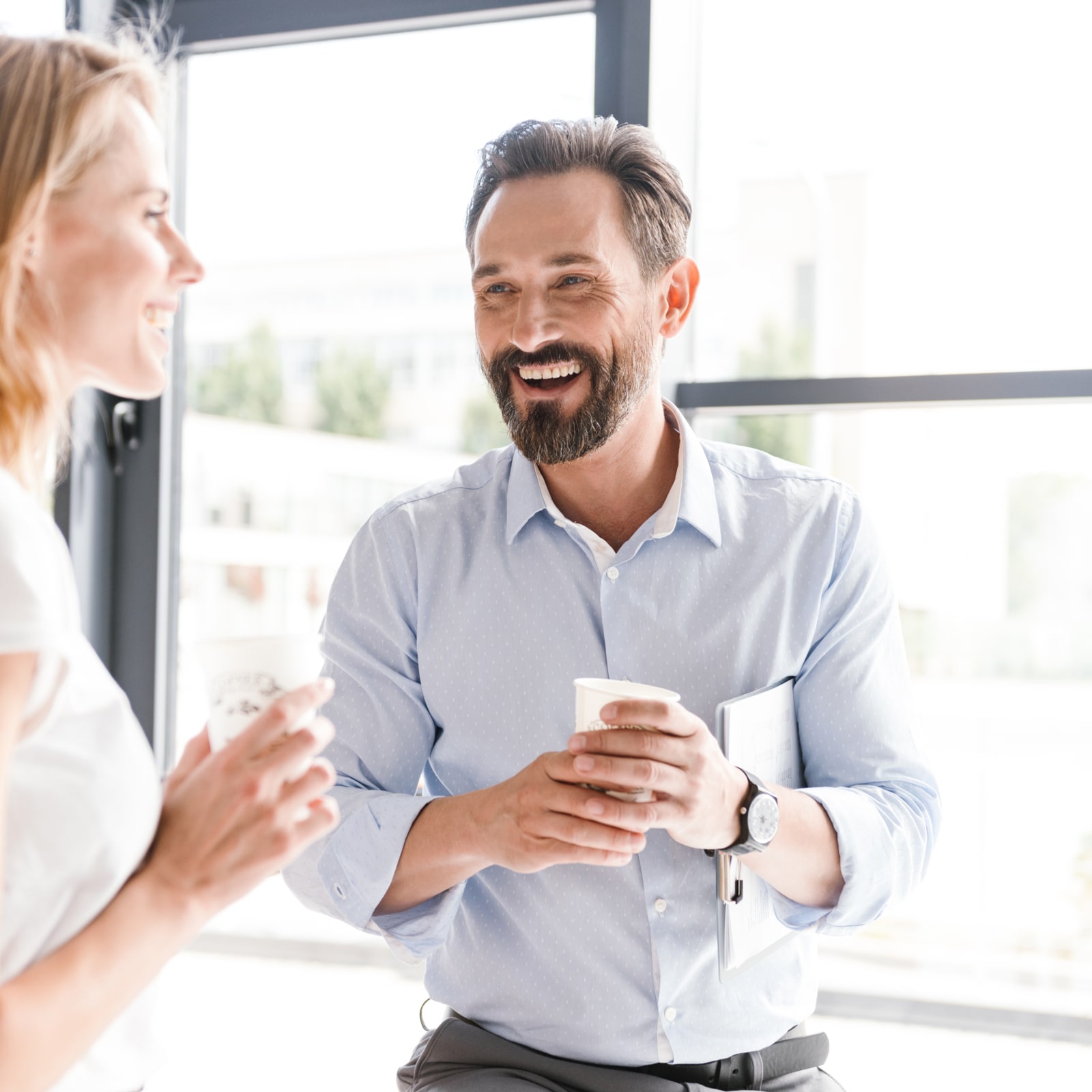 Couple standing at the office window with cups of coffee