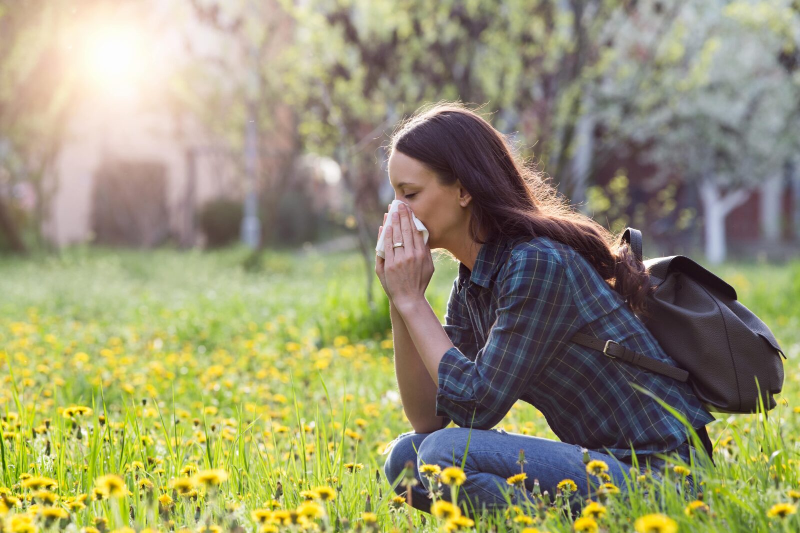 woman sneezing and sitting in a field of weeds