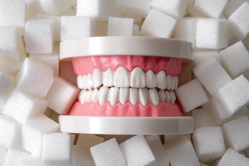 Oral health, tooth decay and sugar destroys the tooth enamel concept with plastic medical model of teeth or dentures surrounded by white sugar cubes