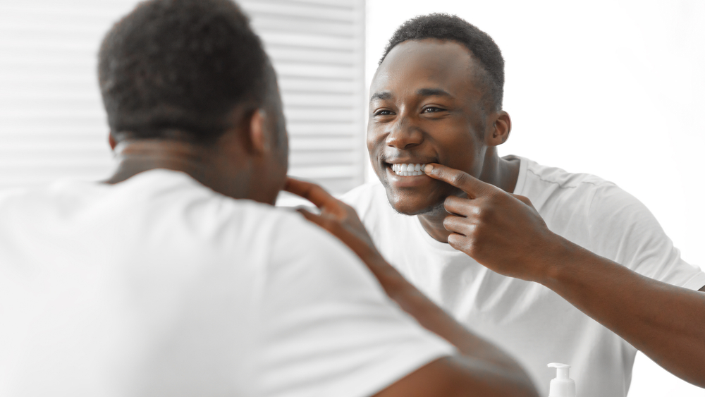 A man smiling in the mirror admiring his smile after a Teeth Whitening session