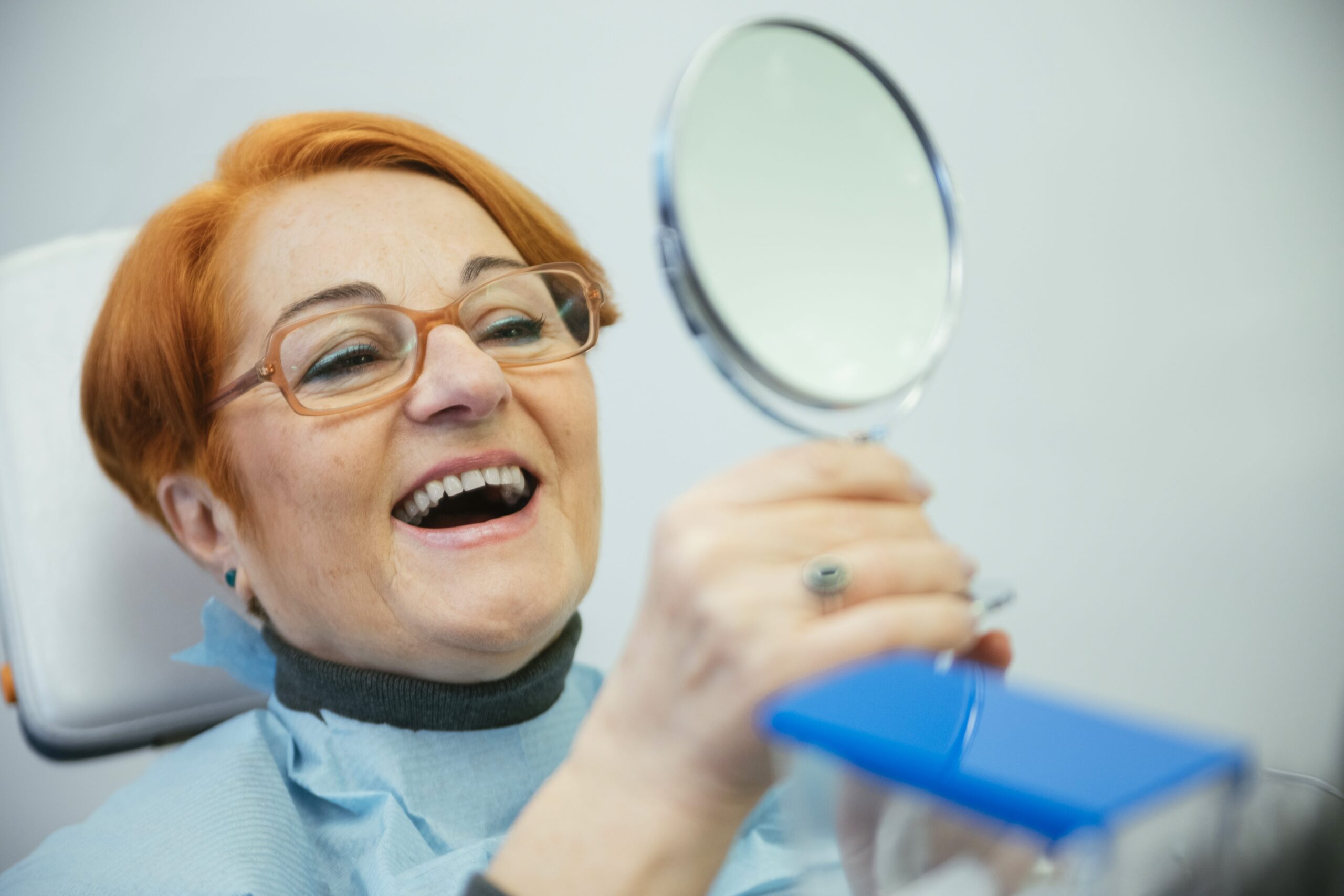 senior woman sitting in dental chair looking at mirror