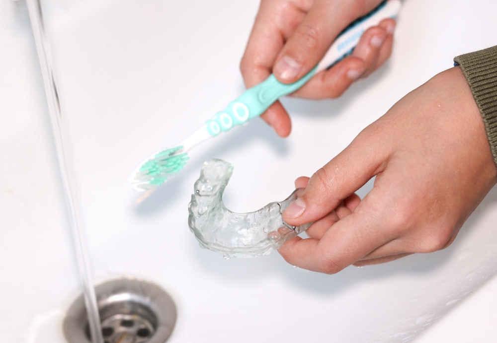 Hand cleaning transparent retainer with toothbrush and toothpaste over sink.