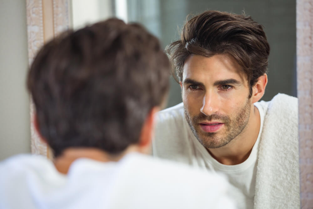 Young man looking himself in bathroom mirror