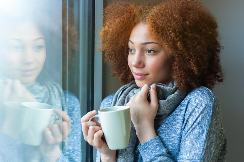 girl drinking a hot beverage and looking through a window