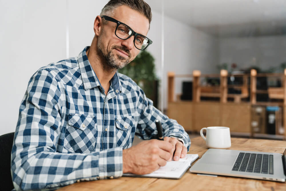 Pleased man writing down notes while working