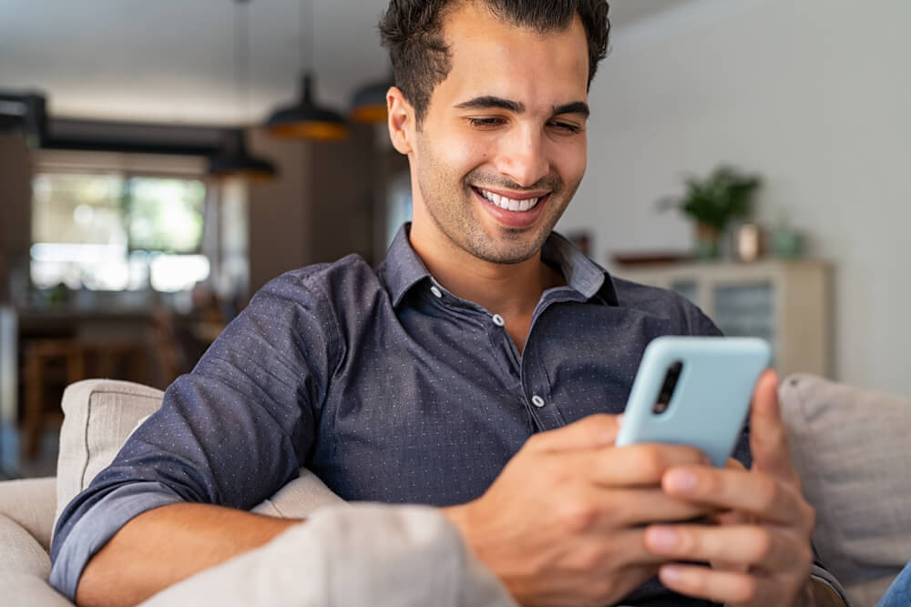 Cheerful man using smartphone while sitting on sofa