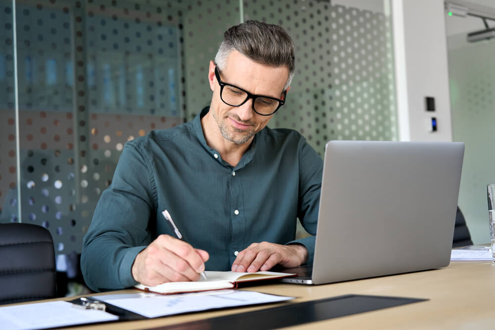 man using laptop writing notes in notebook