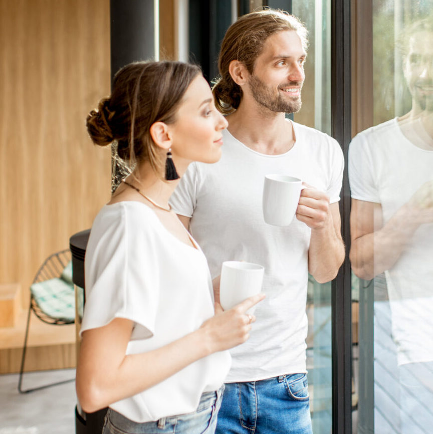 happy couple standing with cups near the window