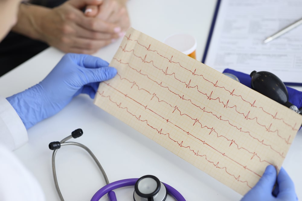 Doctor's hands hold result of the cardiogram next to patient sitting