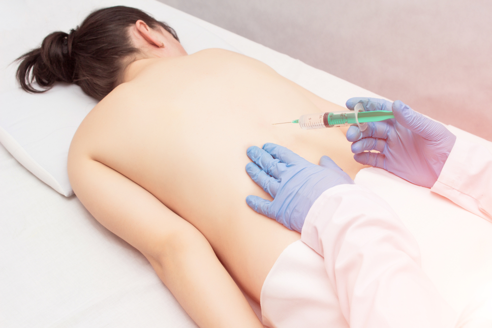 The doctor makes a patient a girl an injection of a blockage in the spine to eliminate back pain