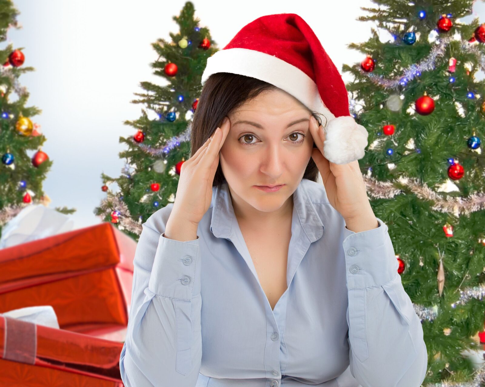 A stressed out woman wearing a Santa had with Christmas trees and gifts in the background