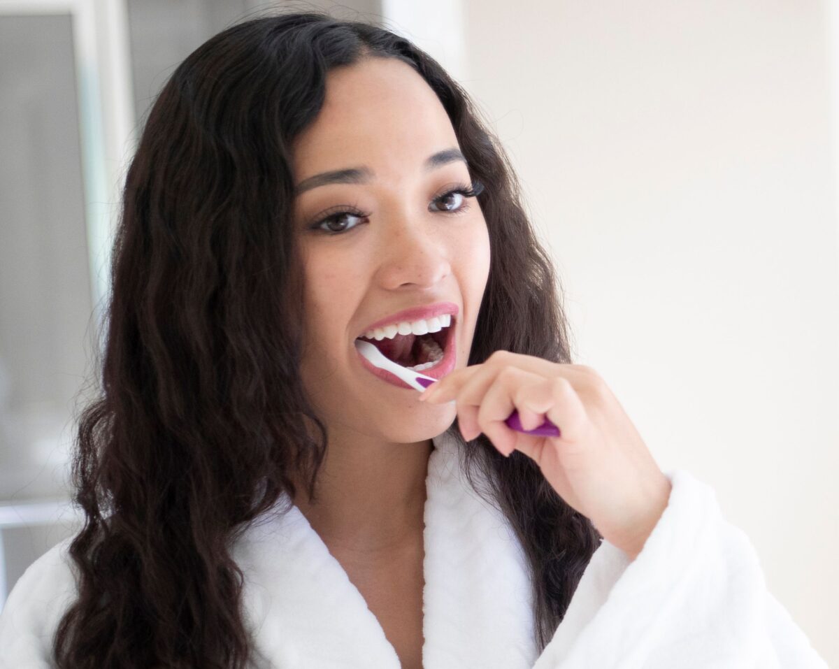 A dark haired young woman brushing her teeth