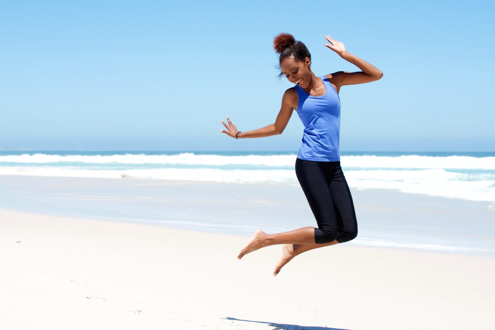 Portrait of young sporty woman jumping with joy at the beach