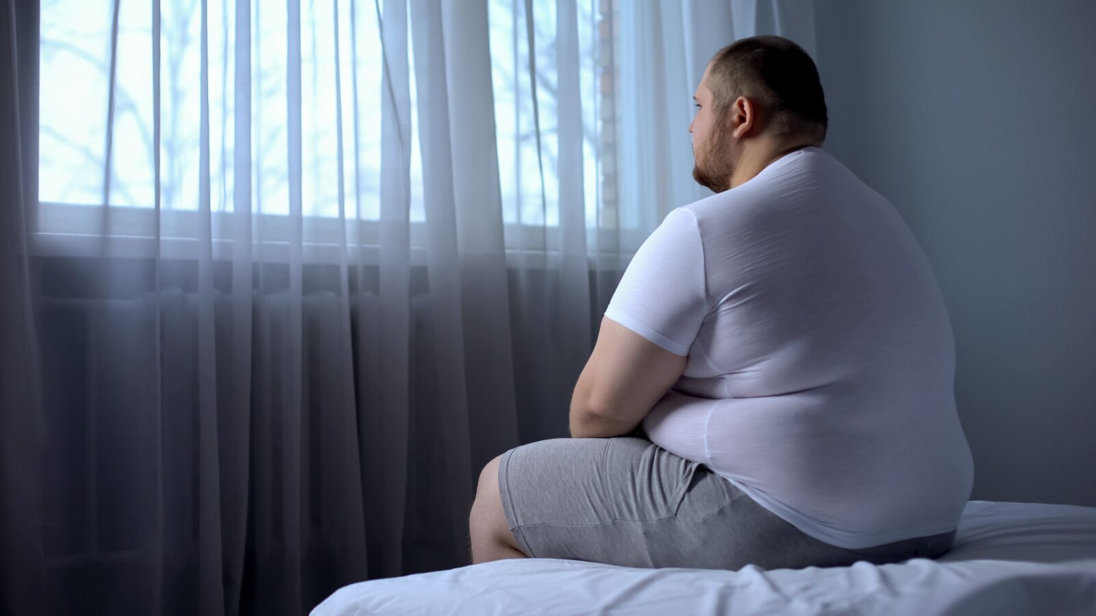 obese man sitting on bed