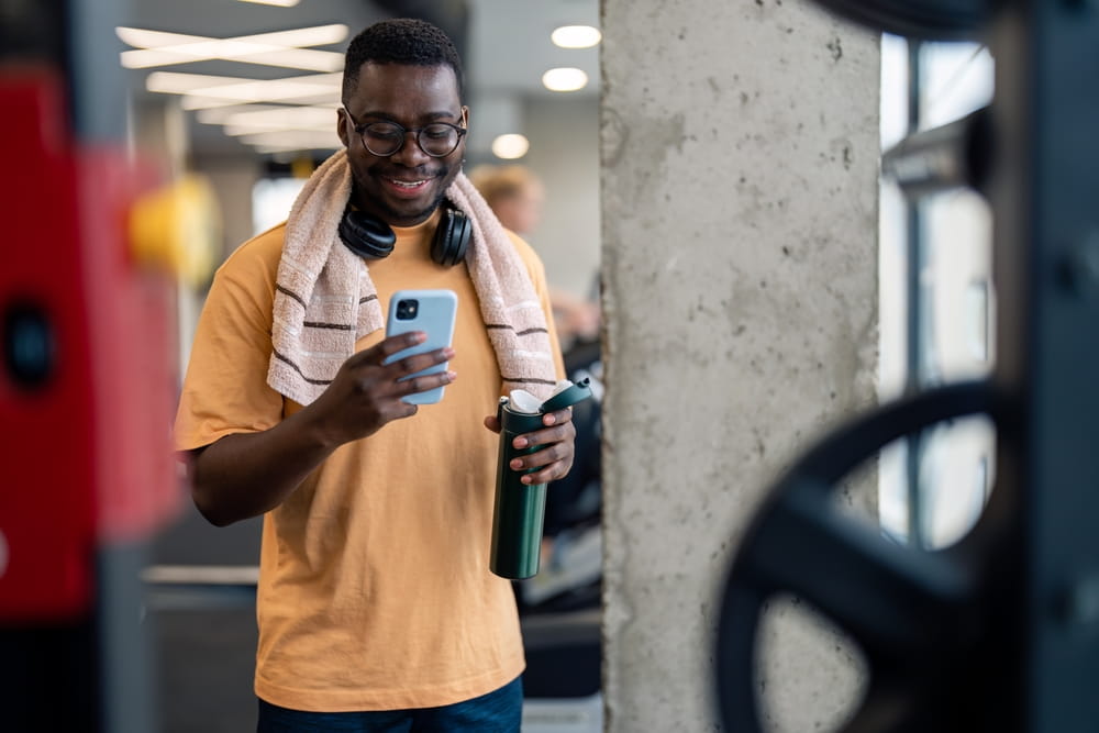 Handsome African American sportsman using mobile phone while taking a break from exercising