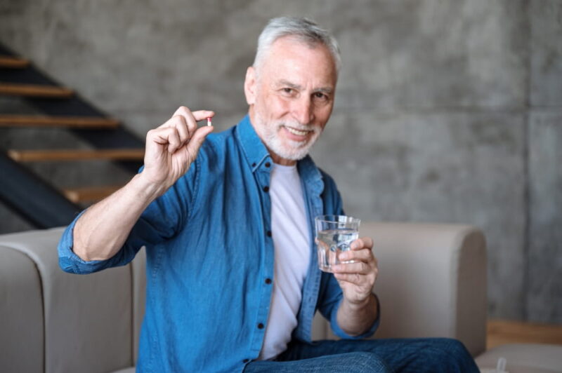 Male holding tablet and glass with water. Intaking capsule with omega3, vitamin D
