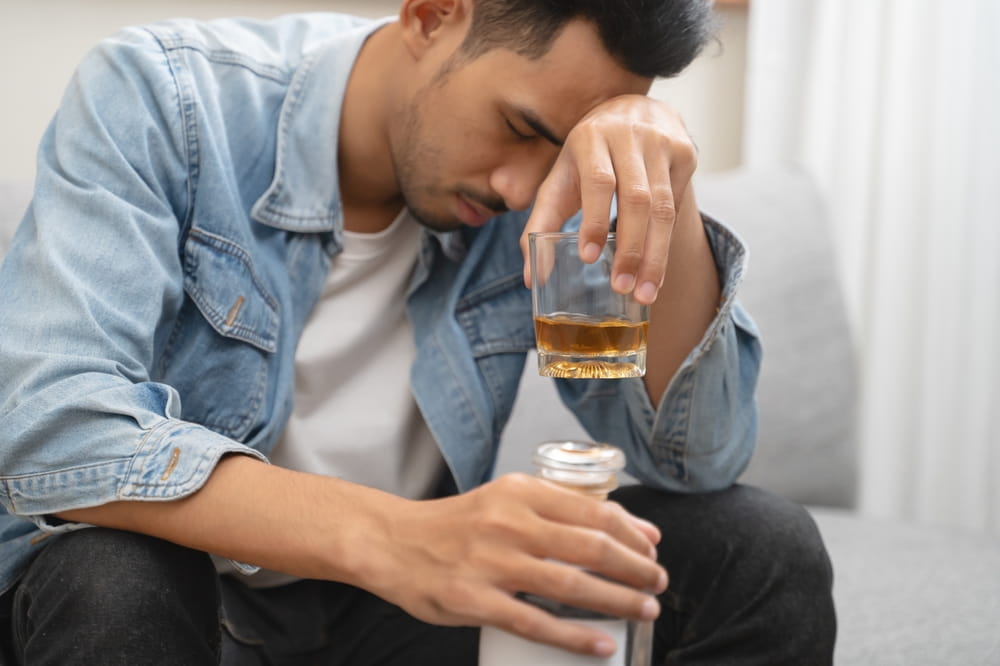 melancholy young Asian man drinks alcoholic whisky alone at home feeling dizzy after drunk