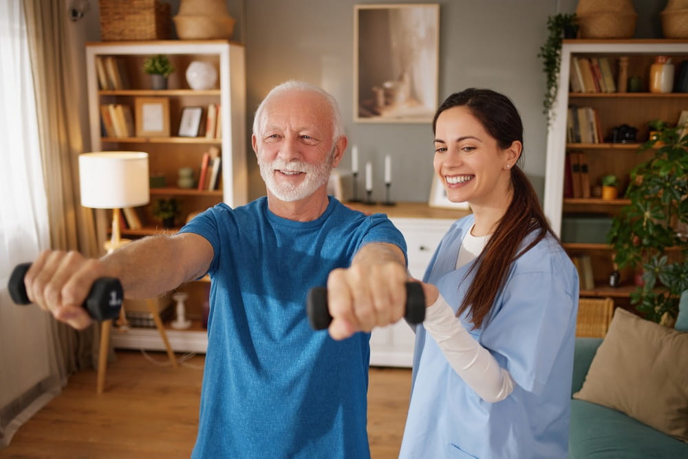 Home health nurse guides senior man in performing exercises with weights in his living room