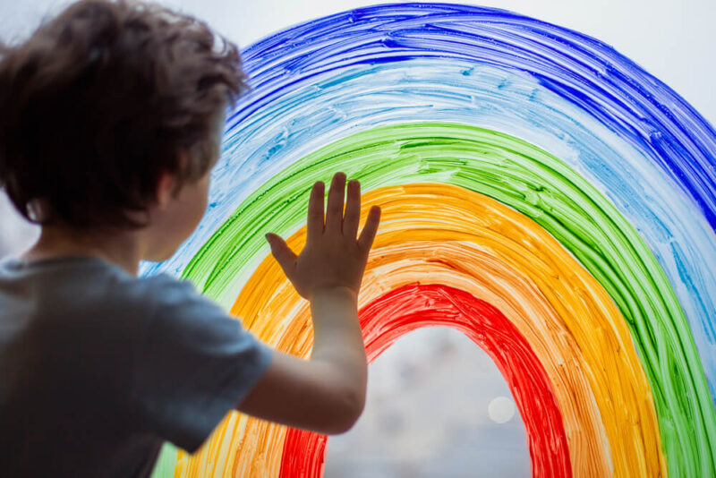 child at home draws a rainbow on the window.