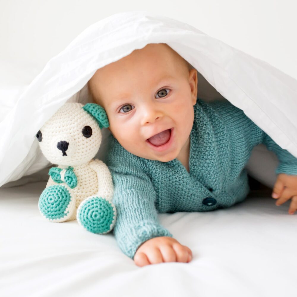 child in knitted sweater, holding knitted toy, smiling happily