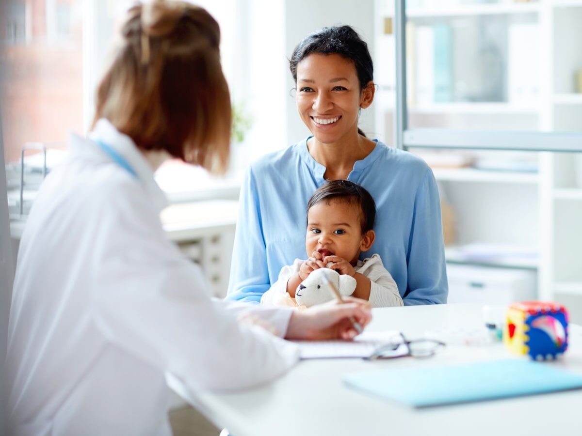 Smiling young mother sitting together with her baby and talking to the doctor