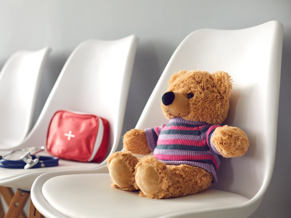 First-aid kit, stethoscope and cute teddy bear on white chairs