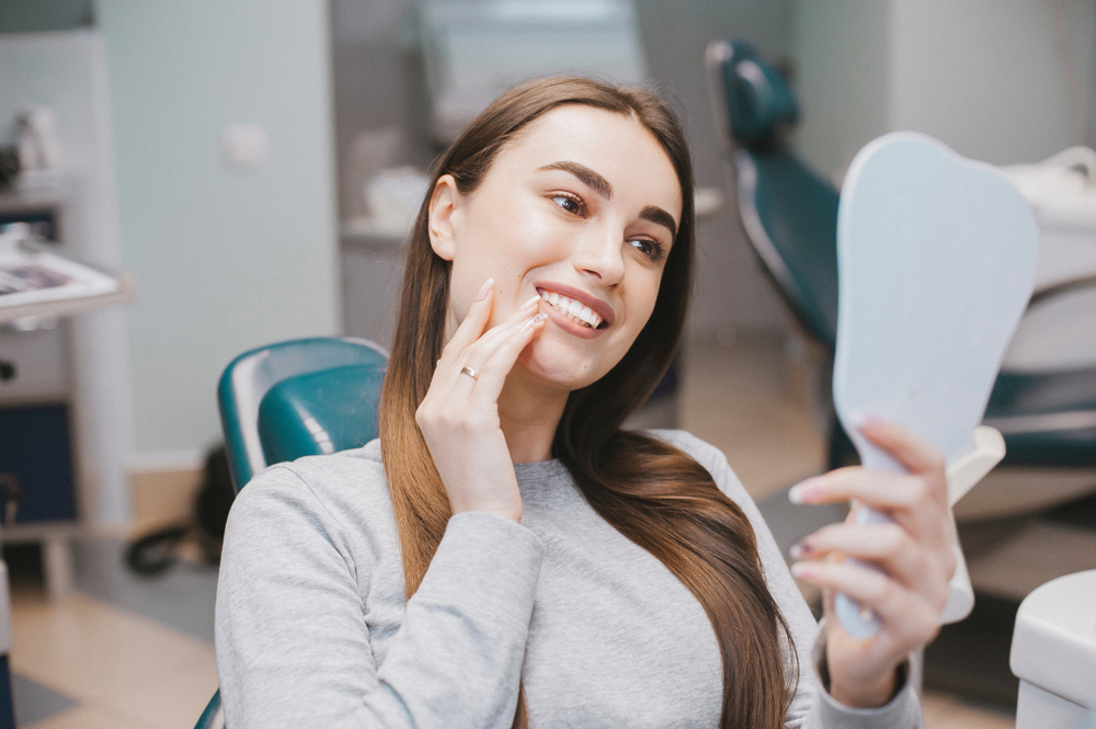 Woman smiling in a hand held mirror after receiving dental Restorations
