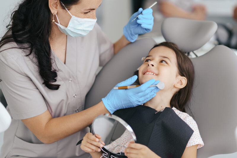 Cute little girl sitting on a modern dental chair and having dental consultation with dentist