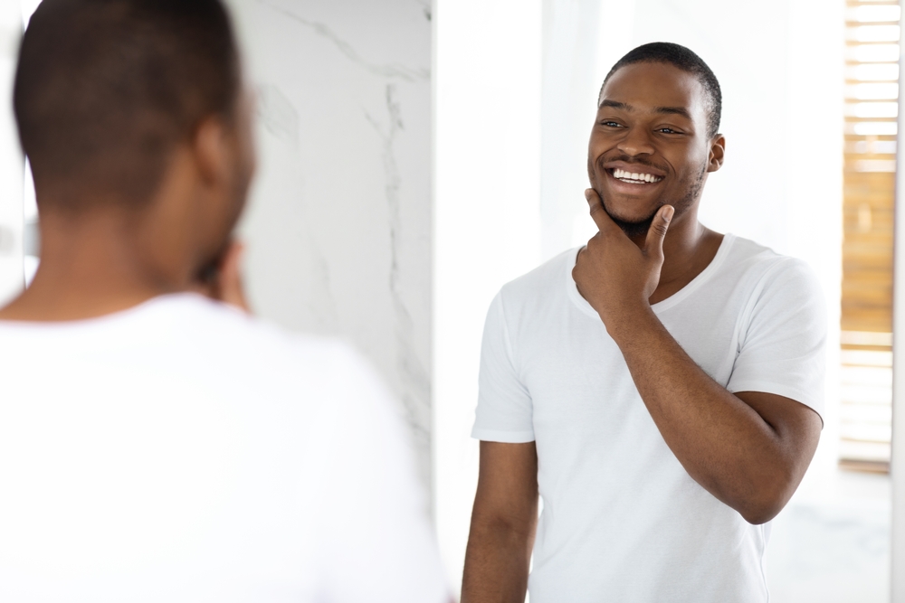 Man smiling in the mirror after receiving a teeth whitening treatment