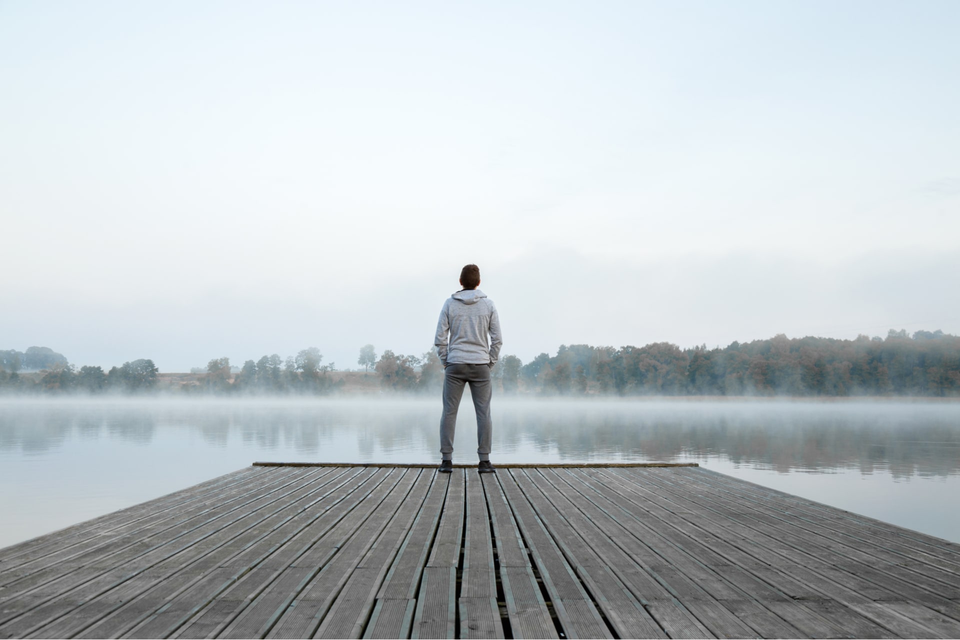 Young man standing alone on wooden footbridge and staring at lake