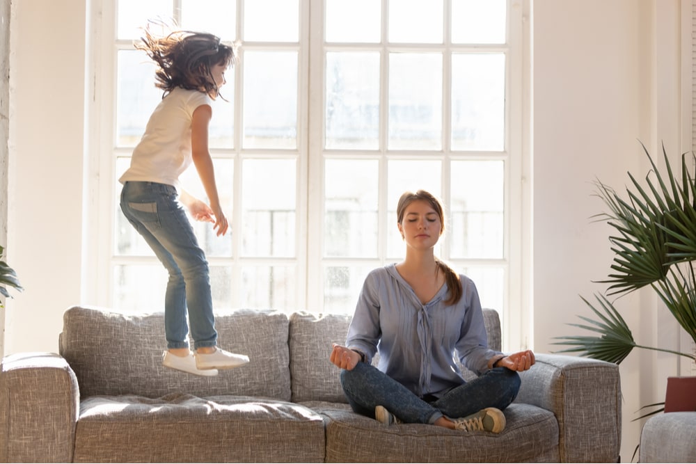 Young mom sit on couch at home meditating in lotus position
